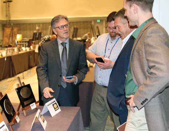 (four men looking at items on a display table)