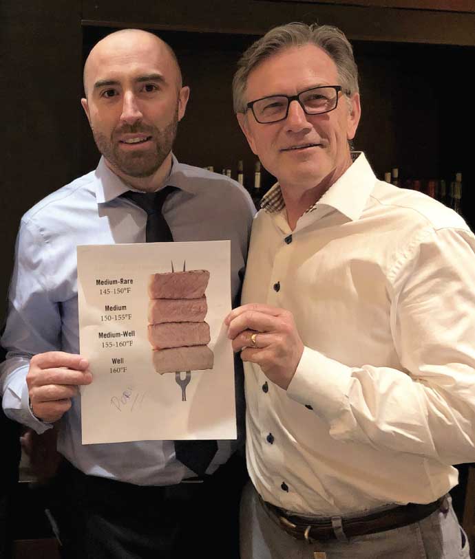 Two men holding a poster showing examplesof pork cooked to different temperatures