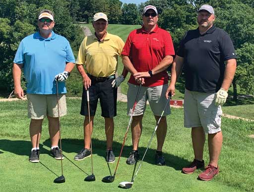 Four people standing outdoors with golfing equipment