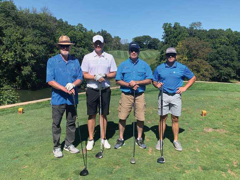 Four people standing on a putting green holding golf clubs