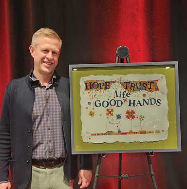 Person standing next to framed artwork with text reading in part, "HOPE TRUST life GOOD HANDS"