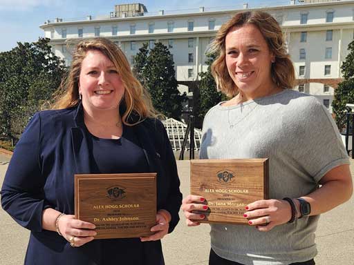 Two women holding award plaques standing side-by-side outdoors