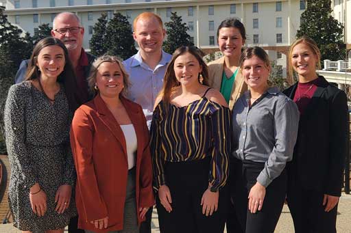 Eight people standing side-by-side facing the camera outdoors