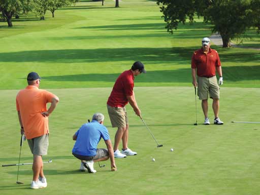 Four people on a putting green; one putting; the others watching intently